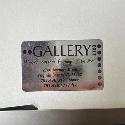 A rectangular metallic custom frame label with rounded corners, featuring the word 'GALLERY' and contact details for a Virginia Beach art gallery, shown against a light textured wall.