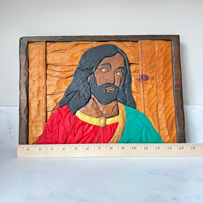 Wooden carving of a religious figure with a ruler for scale on a white background
