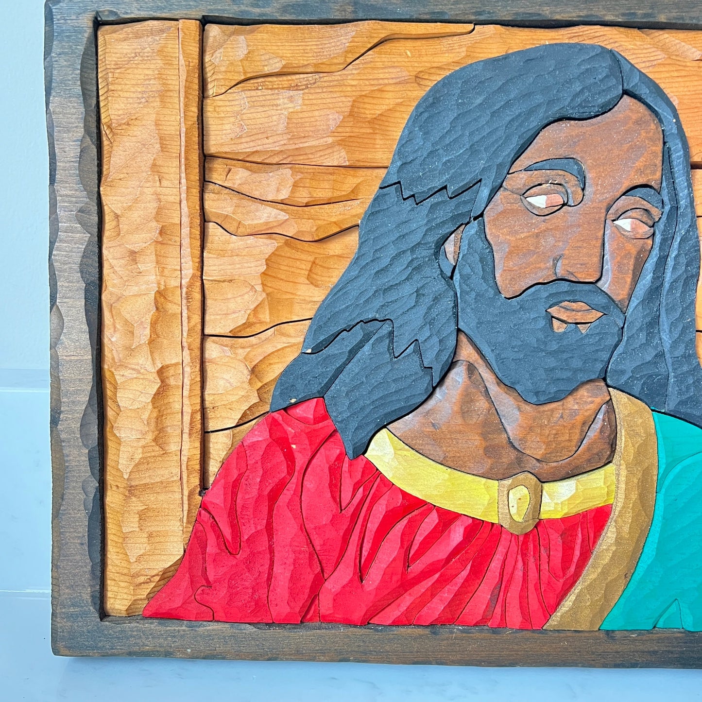 Wooden carving of a religious figure with long hair and a beard, wearing a red robe and a yellow collar.