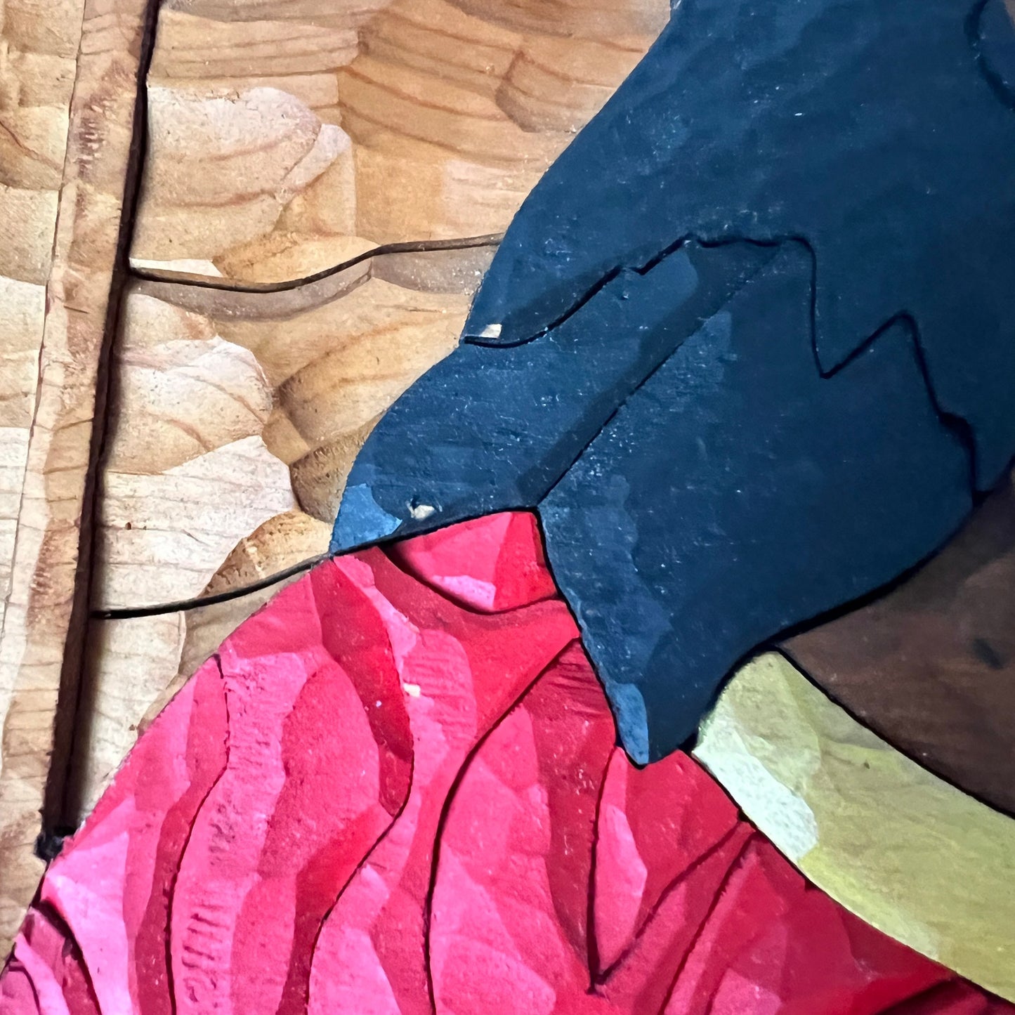 Close-up of a pink wood with a blue and yellow pattern on a wooden surface showing 3 areas where paint is chipped
