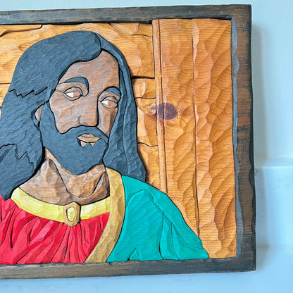 Wooden carving of a religious figure with a blue beard and red robe on a wooden panel.