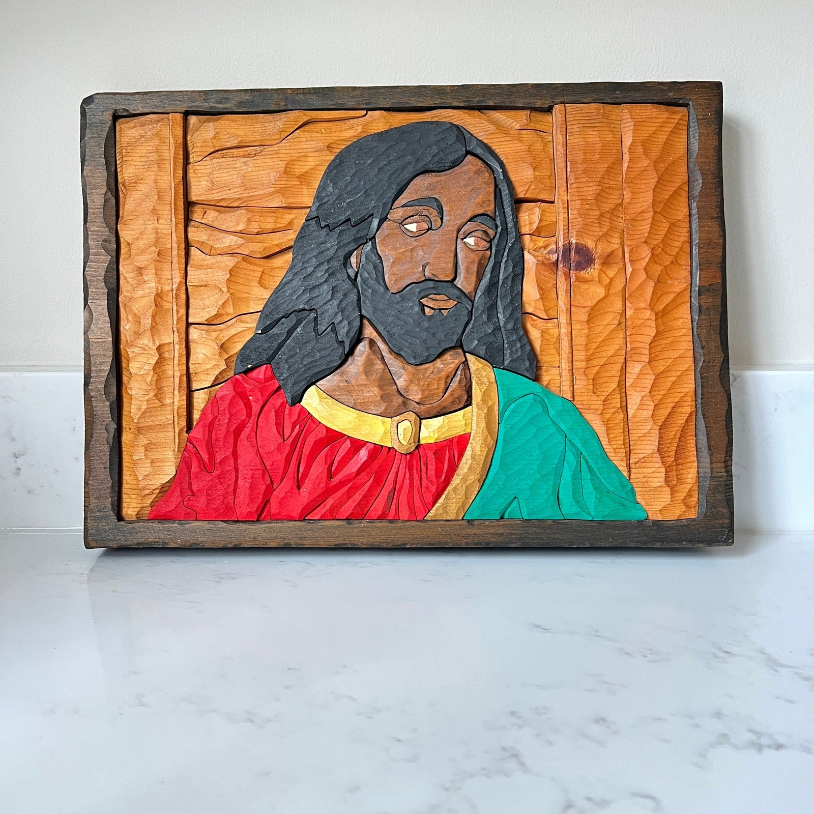 Wooden relief sculpture of a religious figure with a colorful robe on a white marble surface.