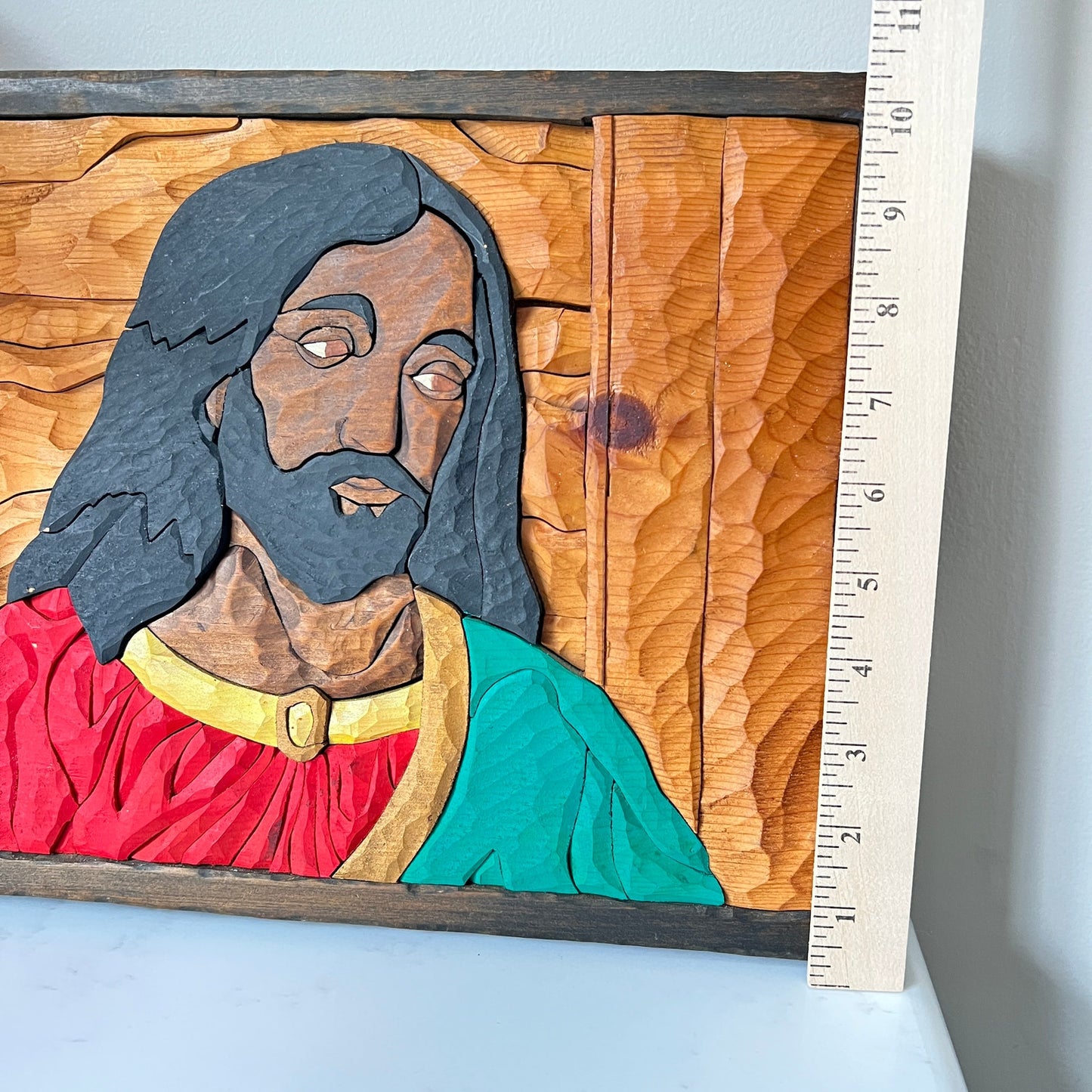 Wooden carving of a religious figure with a ruler for scale on a light blue background