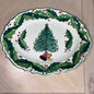 An oval white ceramic Christmas serving platter with a scalloped edge, decorated with a green holly leaf border and red berries, featuring a central illustration of a decorated Christmas tree with presents.