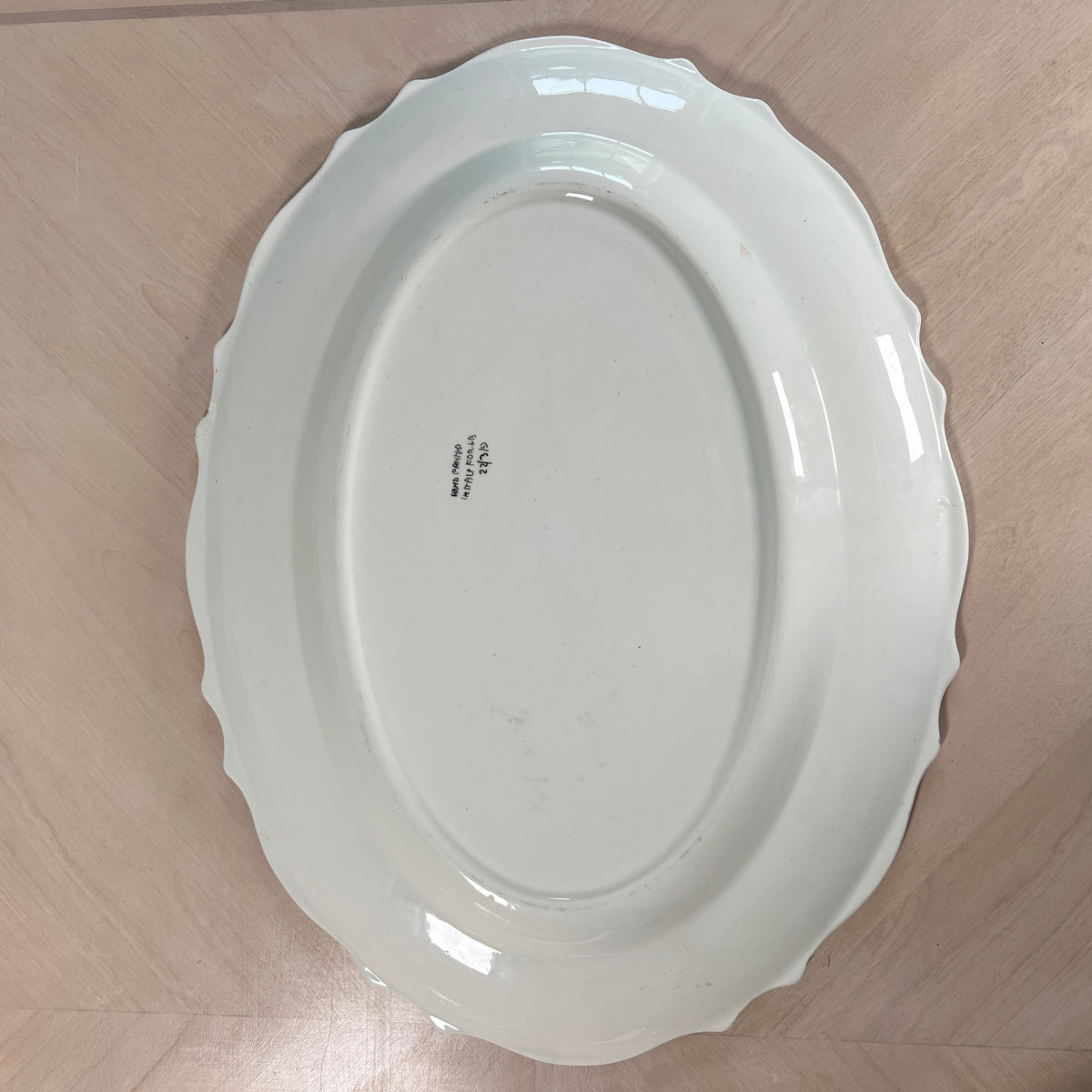 An oval white ceramic serving platter with a scalloped rim, photographed from directly above on a light wood floor.