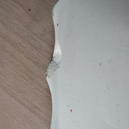 A close-up of a white ceramic or porcelain surface with a rough, chipped edge against a light wood grain background.