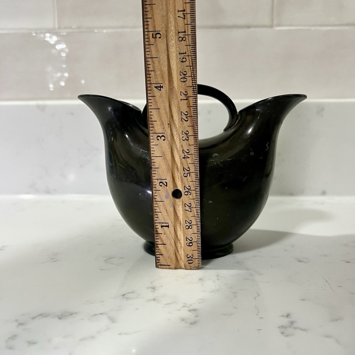 Double Spout vase with a wooden ruler for scale on a white marble surface.