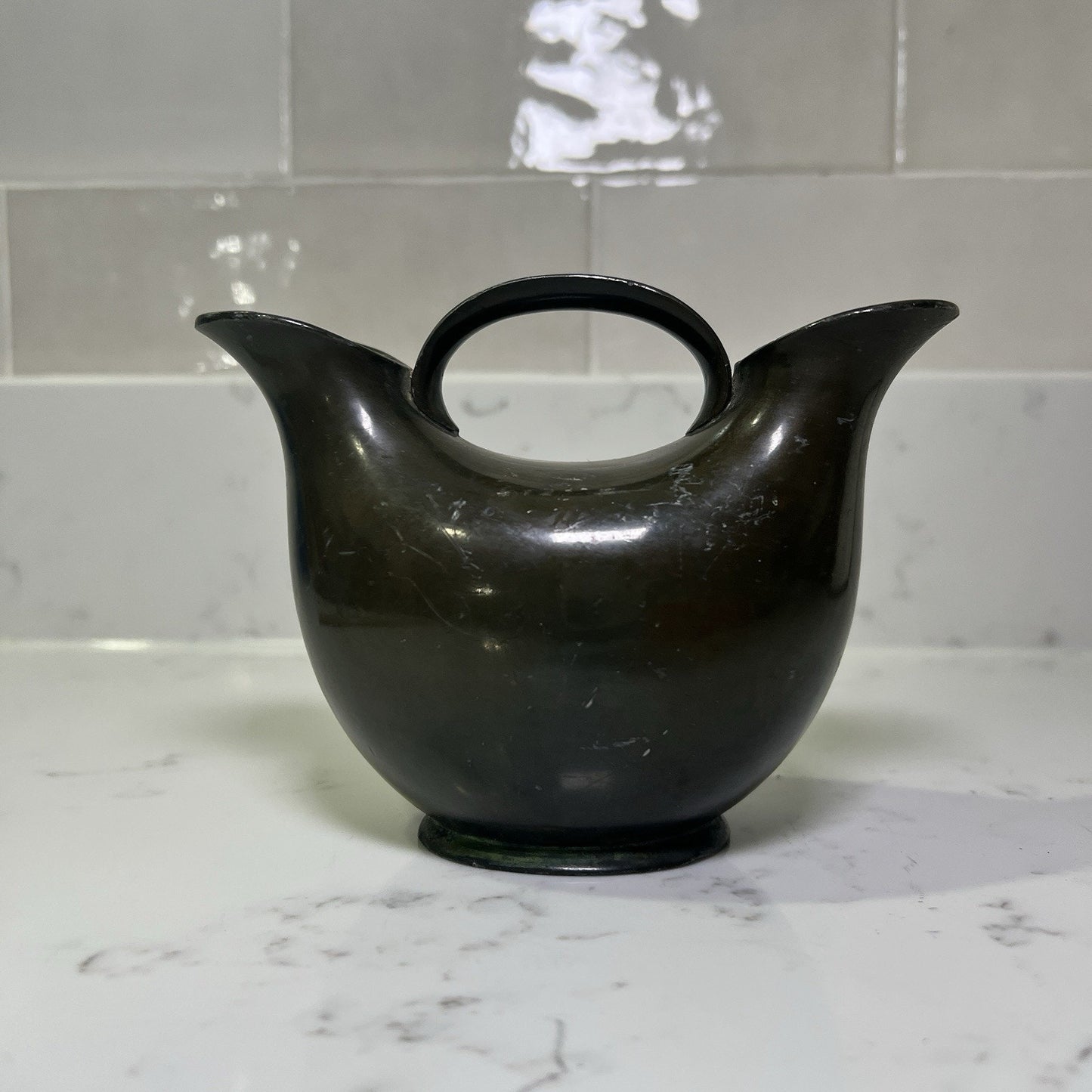 Bronze Double spout vase on a marble countertop with a tiled wall background