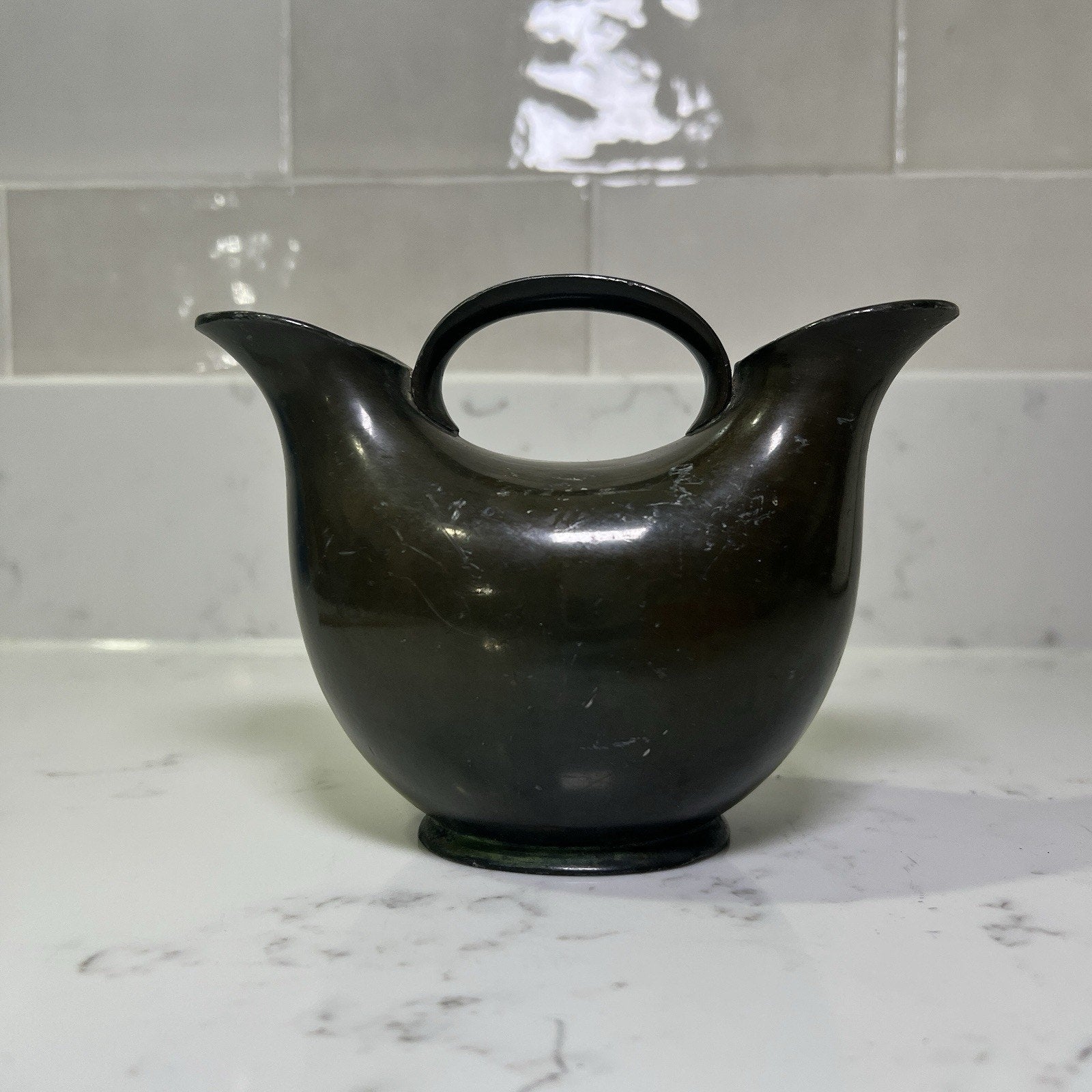 Bronze Double spout vase on a marble countertop with a tiled wall background