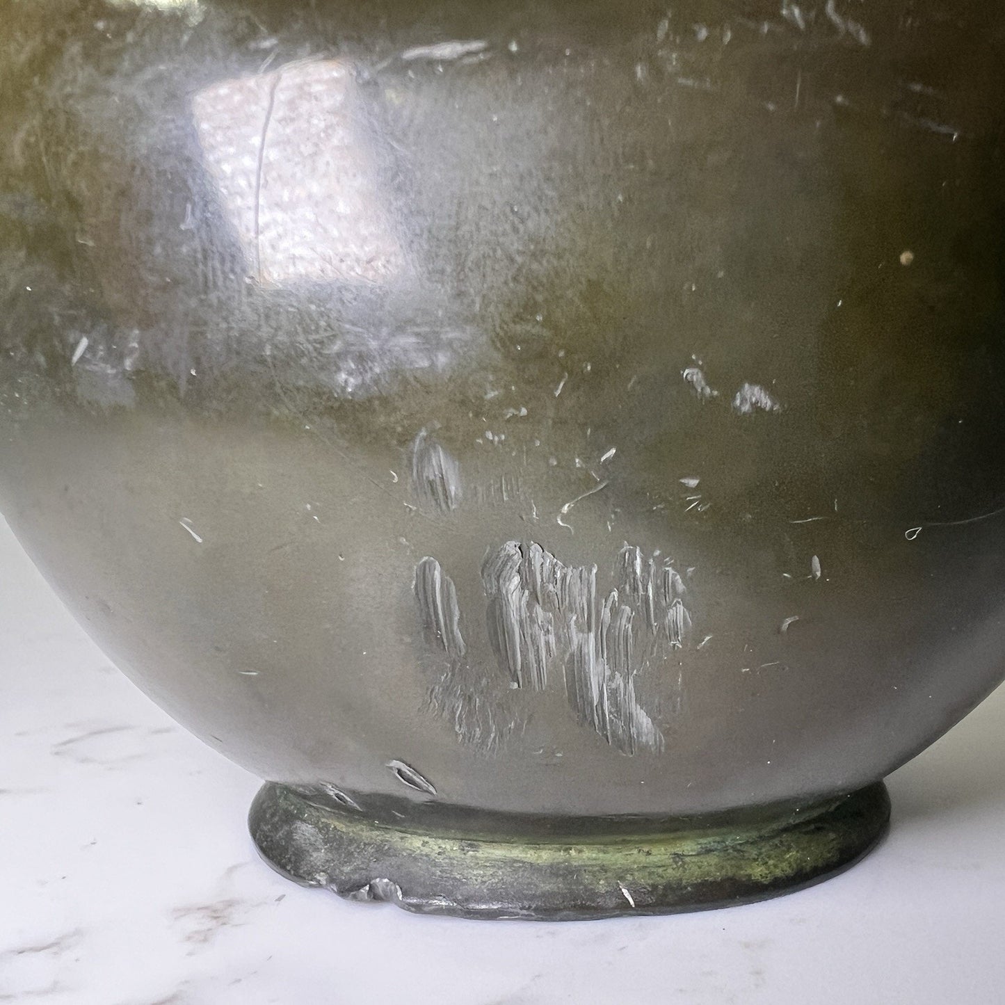 Bronze vase with dent and scuff marks on a marble background