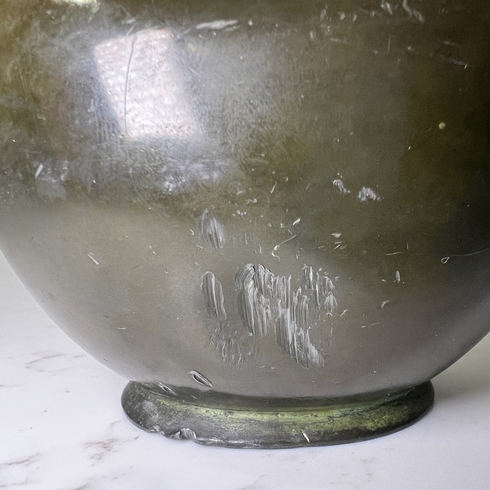 Bronze vase with dent and scuff marks on a marble background