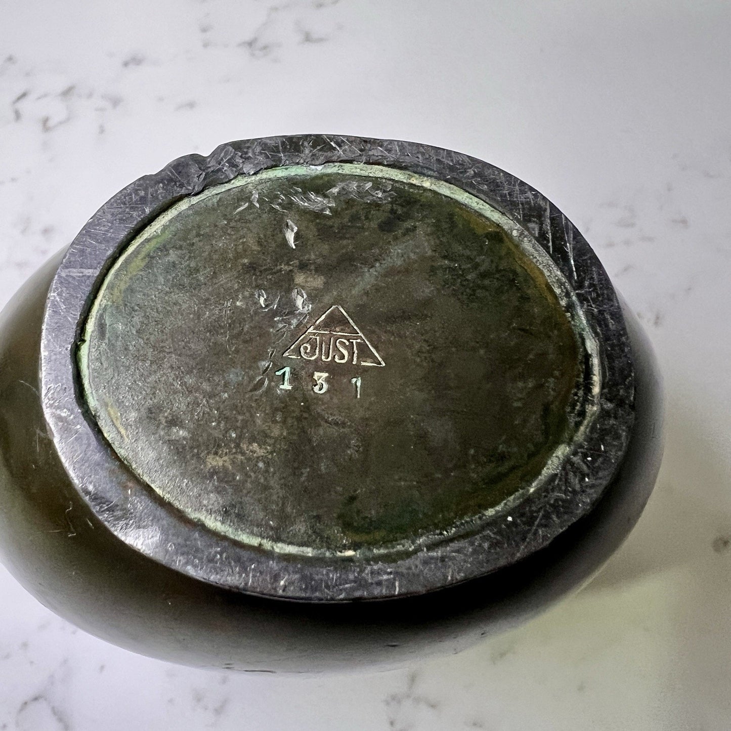 bottom of Bronze vase with 'JUST'  engraving on a marble surface