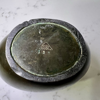bottom of Bronze vase with 'JUST'  engraving on a marble surface