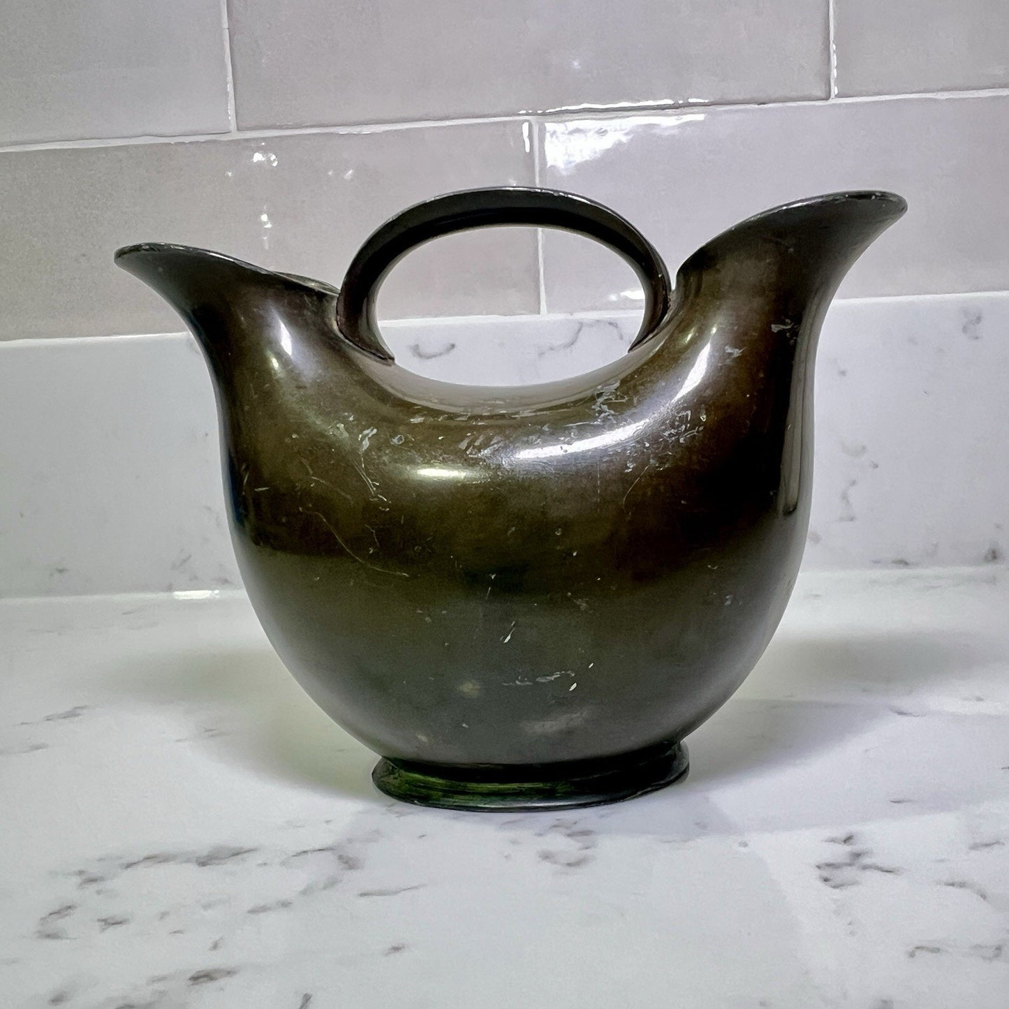 modern-double-spout-metal-vase on a marble countertop with a tiled wall background