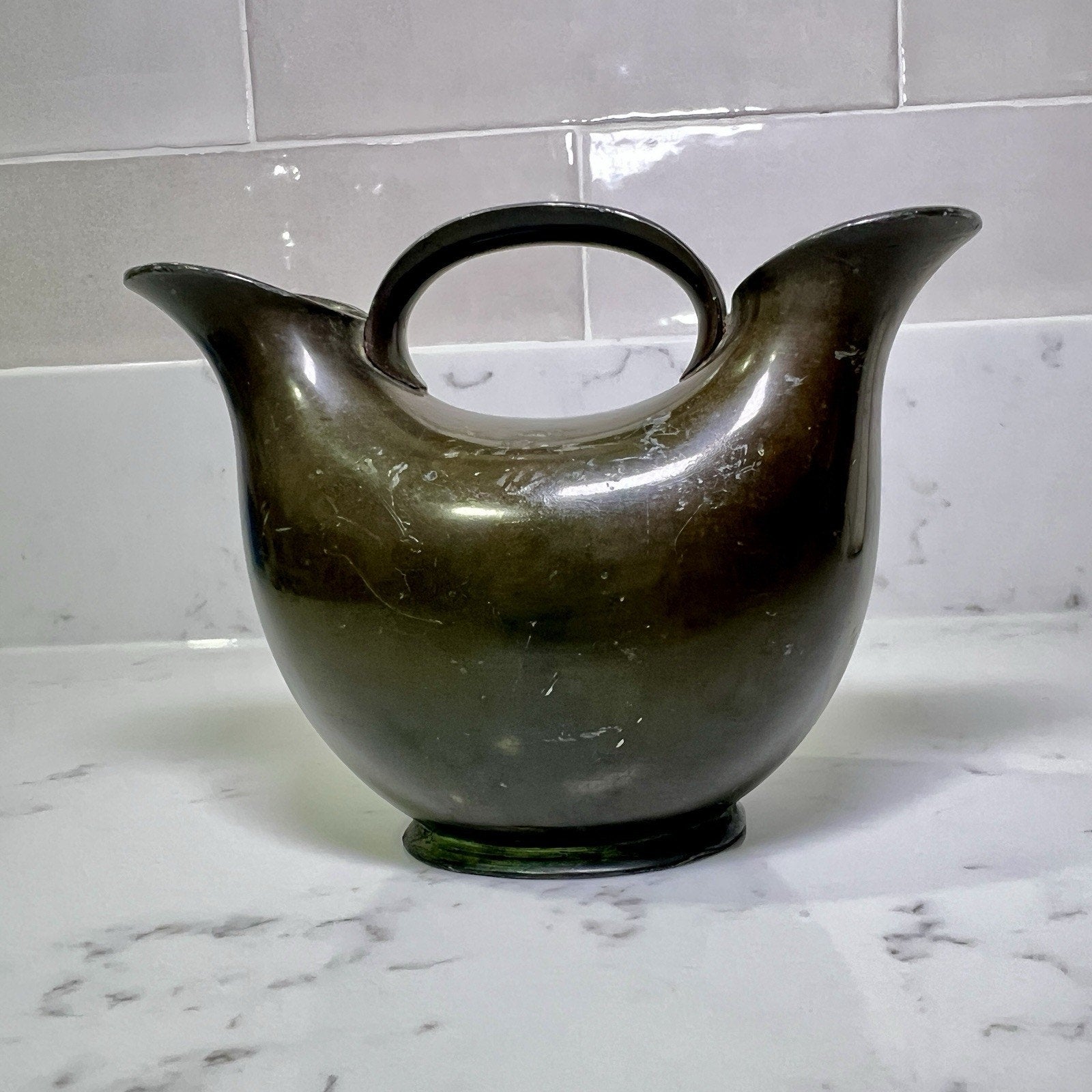 modern-double-spout-metal-vase on a marble countertop with a tiled wall background