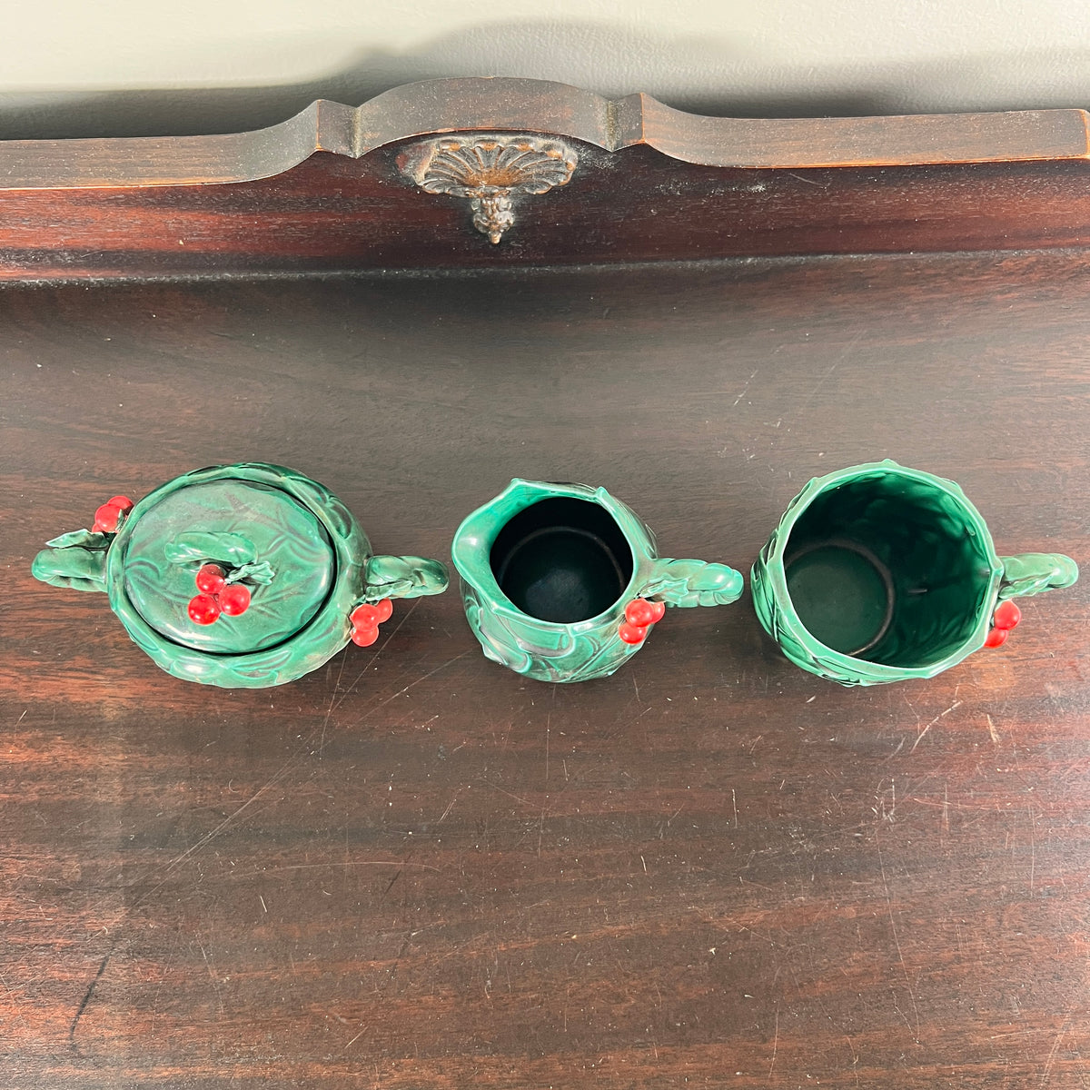 Three vintage green ceramic tea or coffee cups with red berry accents, arranged on a dark wooden surface.