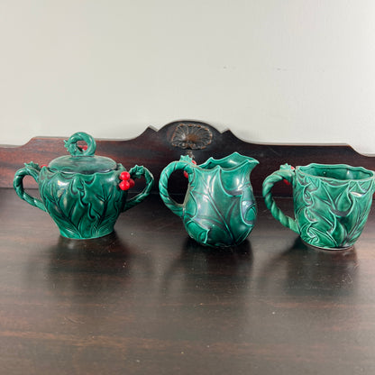 Three glossy green ceramic tea or coffee cups shaped like leaves, arranged on a dark wooden table against a light wall.
