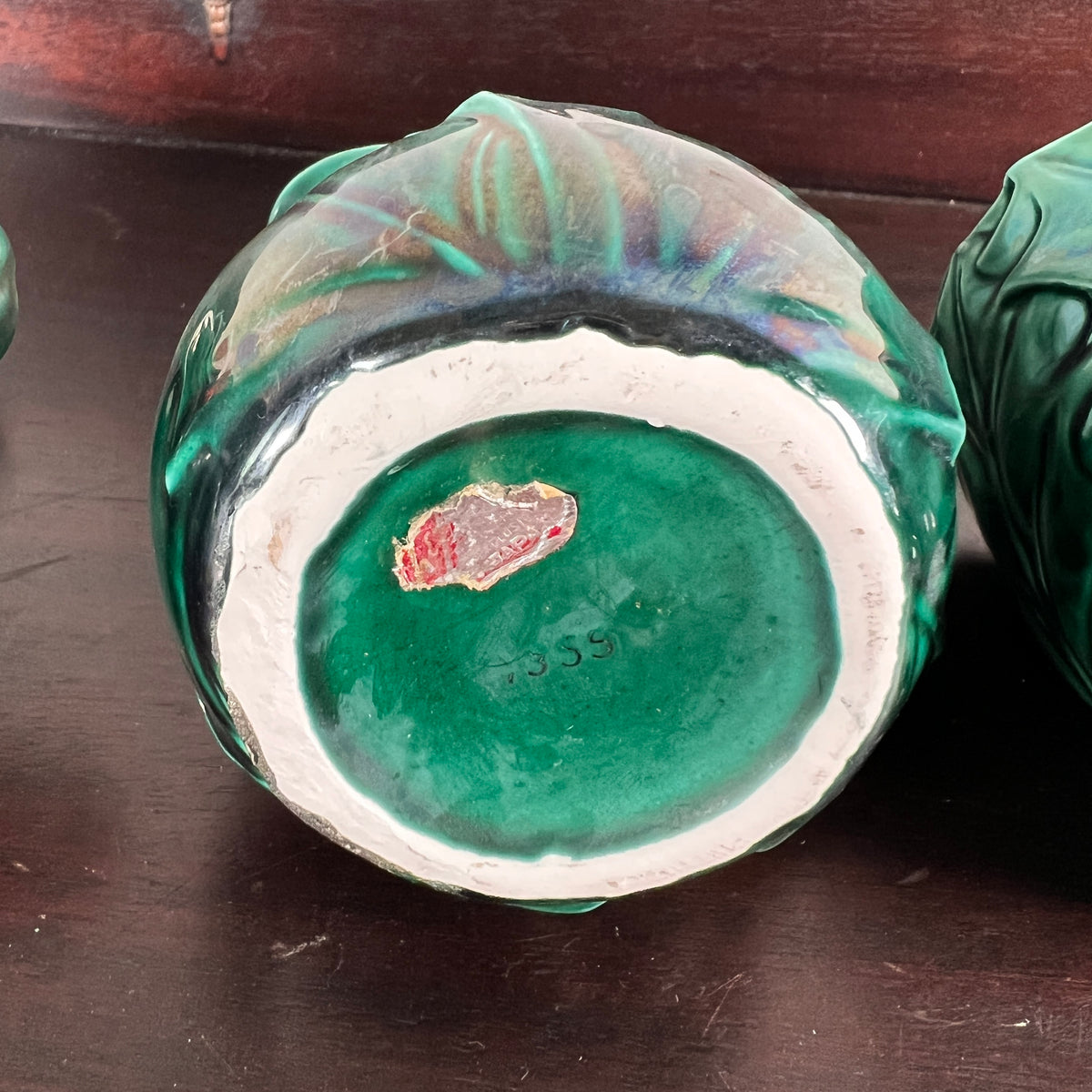 A close-up of the bottom of a green glazed ceramic bowl or vase, showing a white inner rim and a small red chip on the green base, set on a dark wooden surface.