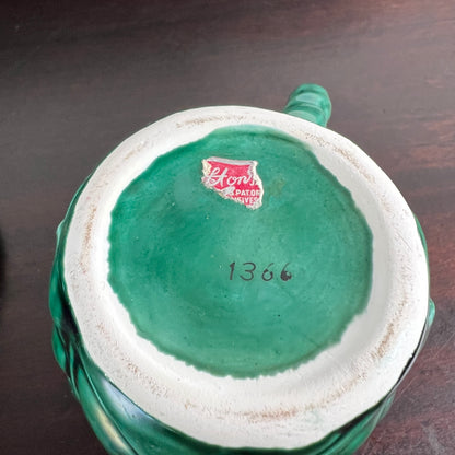The bottom of a vintage green ceramic pitcher or mug, showing a white glazed interior base with a red 'Kenvor' logo sticker and the handwritten number '1366'.