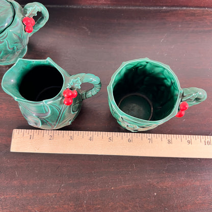 A vintage green ceramic milk pitcher and matching cup with red berry accents, shown on a dark wooden table with a wooden ruler for scale.