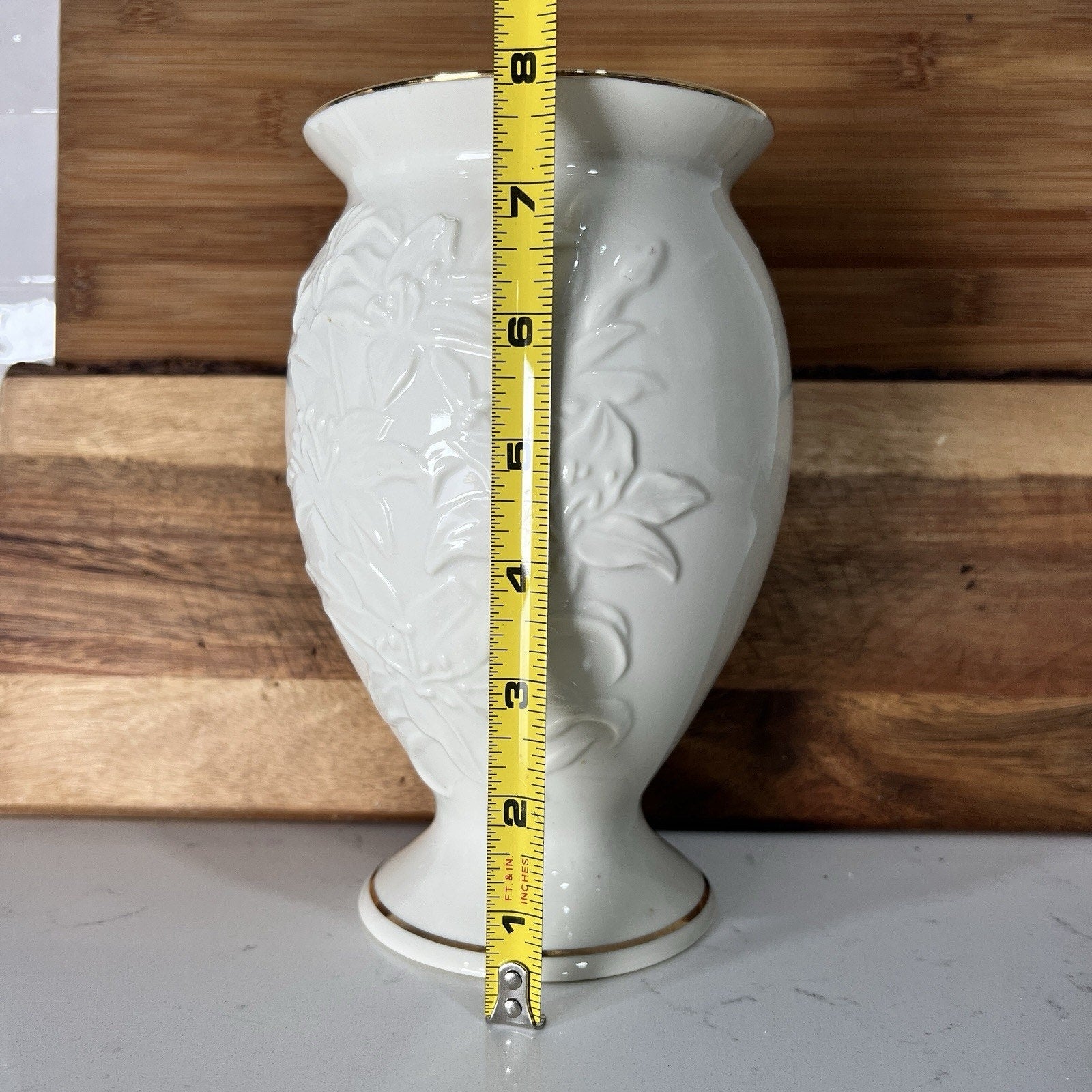 White vase with floral patterns and a tape measure for scale against a wooden background