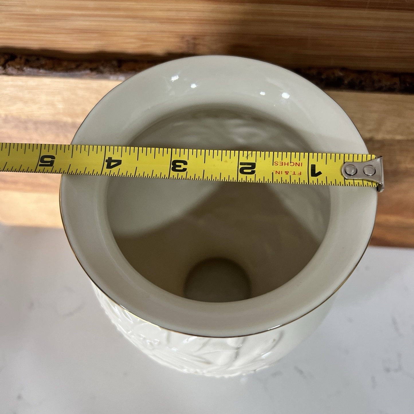 White ceramic vase with a yellow measuring tape around it on a wooden surface.