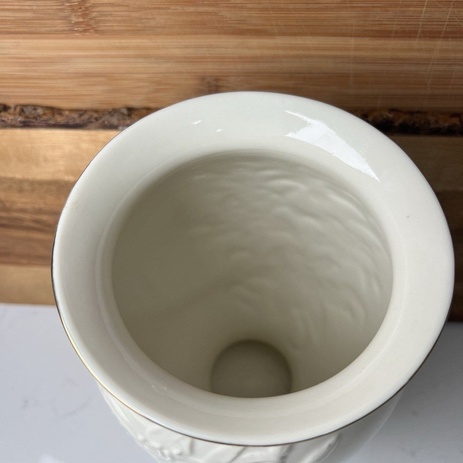 White ceramic vase with gold rim on a wooden surface