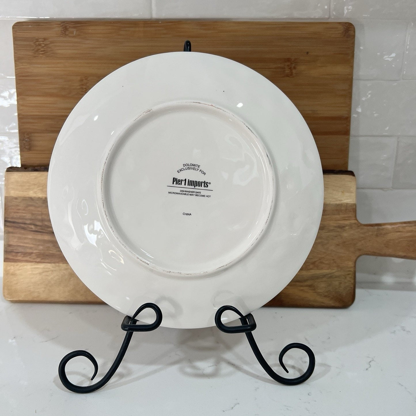 White plate with 'Pier 1' branding on a wooden stand against a tiled wall.