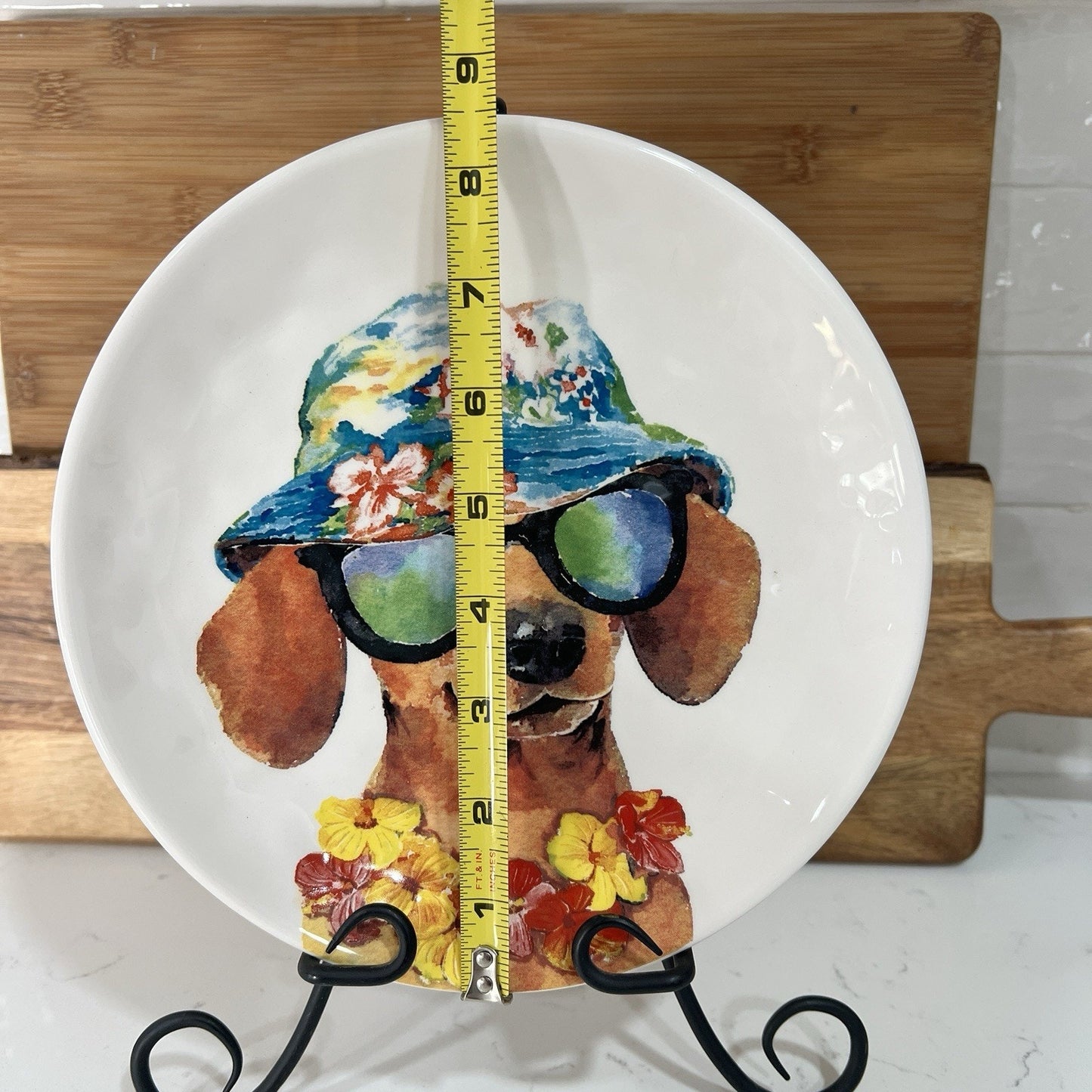 Decorative plate with a dog design, sunglasses, and a measuring tape on a wooden stand.
