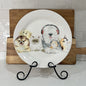 Decorative plate with animal illustrations on a stand against a tiled wall.