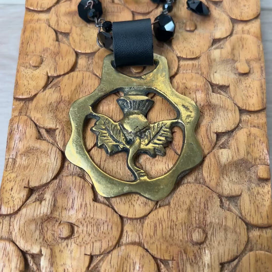 Video of Black beaded necklace with brass medallion with leather attachment on wood with tan background
