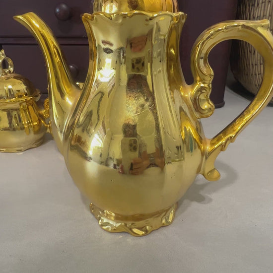 Video of This elegant vintage gold luster tea set brings classic charm and brilliant shine to any display. The complete 15-piece set includes a musical coffee pot, covered sugar bowl, creamer, six teacups, and six matching saucers. The reflective gold finish makes it a standout piece for collectors, tea lovers, and vintage décor enthusiasts.
