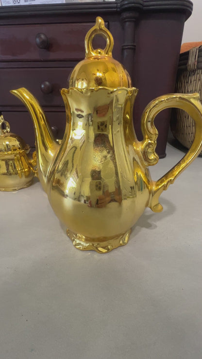 Video of This elegant vintage gold luster tea set brings classic charm and brilliant shine to any display. The complete 15-piece set includes a musical coffee pot, covered sugar bowl, creamer, six teacups, and six matching saucers. The reflective gold finish makes it a standout piece for collectors, tea lovers, and vintage décor enthusiasts.