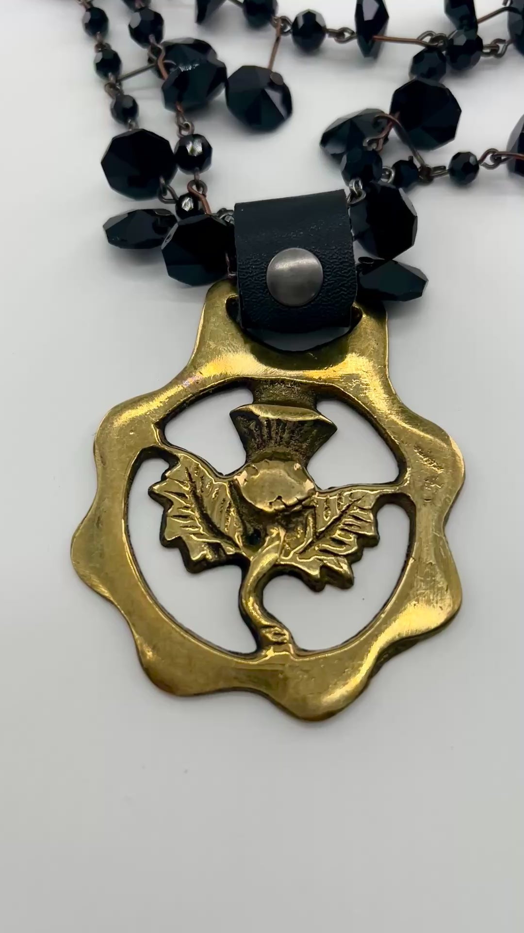 video of Black beaded necklace with brass medallion with leather attachment  with white background