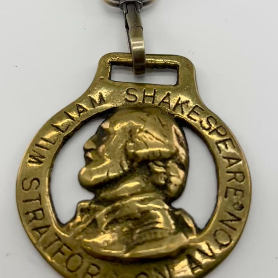 Vintage William Shakespeare horse brass medallion attached to brown leather keychain with brass ring and clip.
