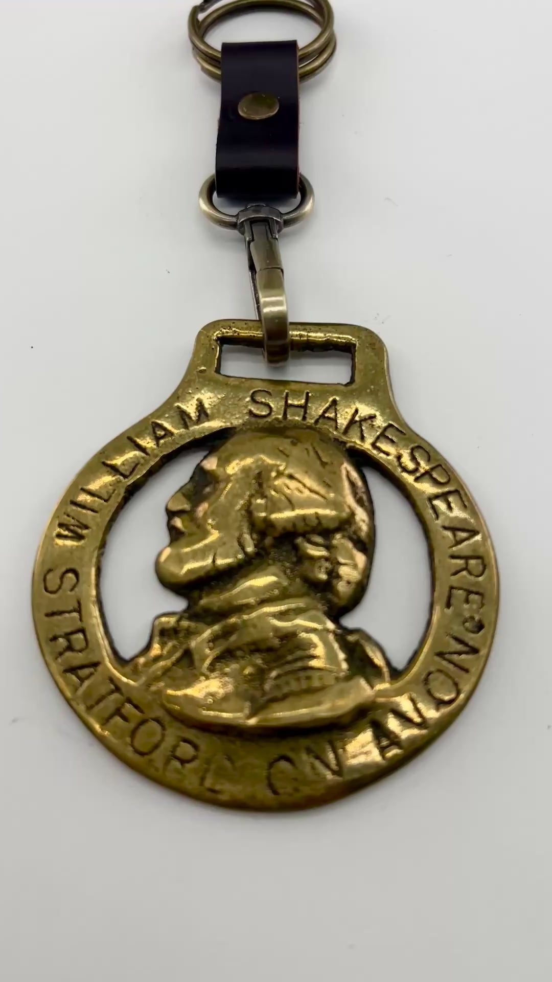 Vintage William Shakespeare horse brass medallion attached to brown leather keychain with brass ring and clip.