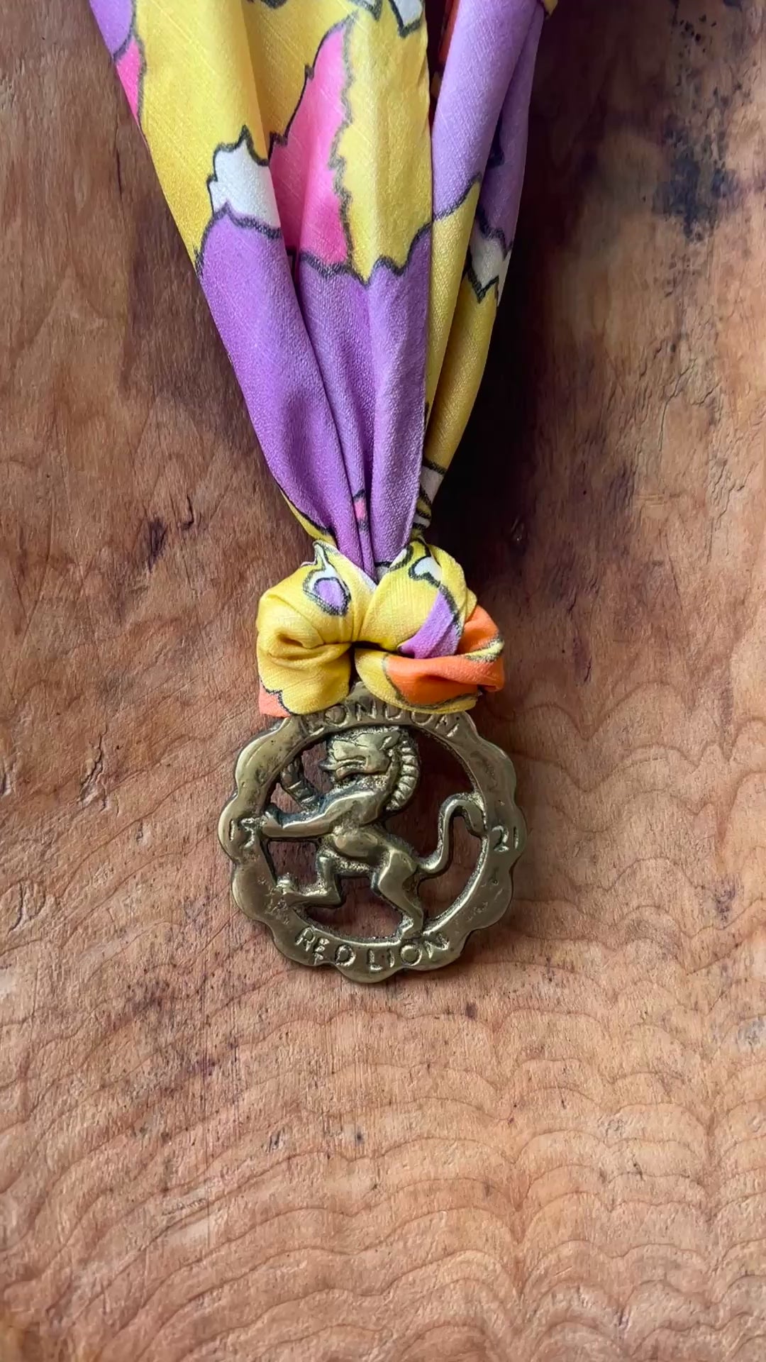 Video of Vintage Red Lion London brass medallion necklace with bright retro floral scarf on wooden surface