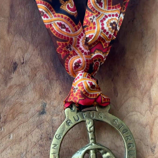 Video Vintage King Rufus Stirrup brass medallion necklace with red paisley scarf, equestrian jewelry on wooden surface