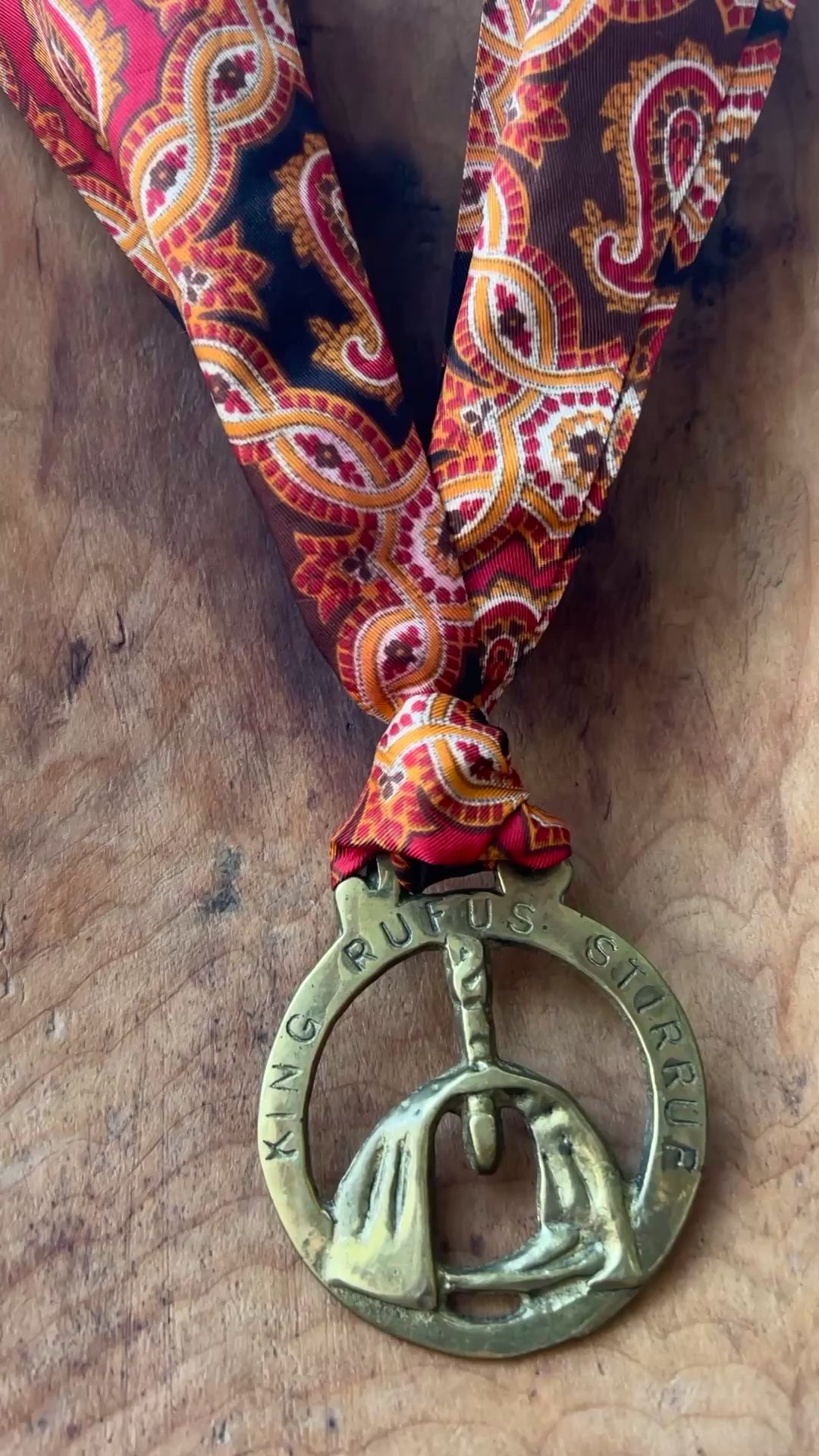 Video Vintage King Rufus Stirrup brass medallion necklace with red paisley scarf, equestrian jewelry on wooden surface