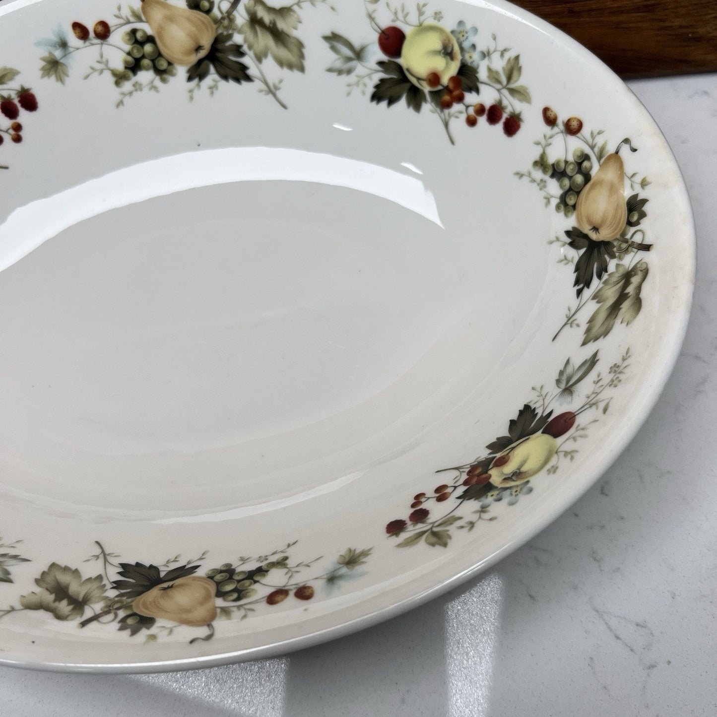 Decorative ceramic plate with fruit and floral pattern on a marble surface
