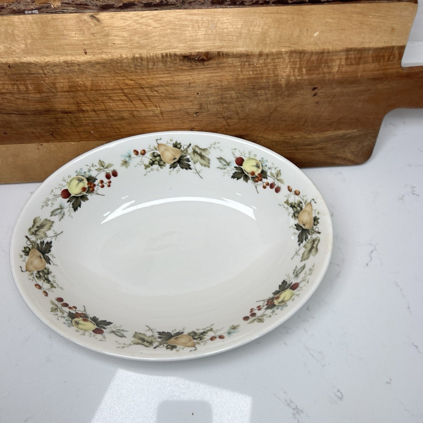 Decorative plate with floral patterns on a white surface with a wooden cutting board in the background