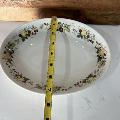 Decorative ceramic bowl with fruit pattern on a white surface, measured by a tape measure.