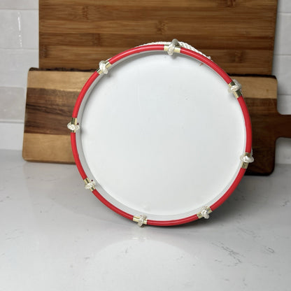 White drum head with red rim and gold hardware on a wooden stand.