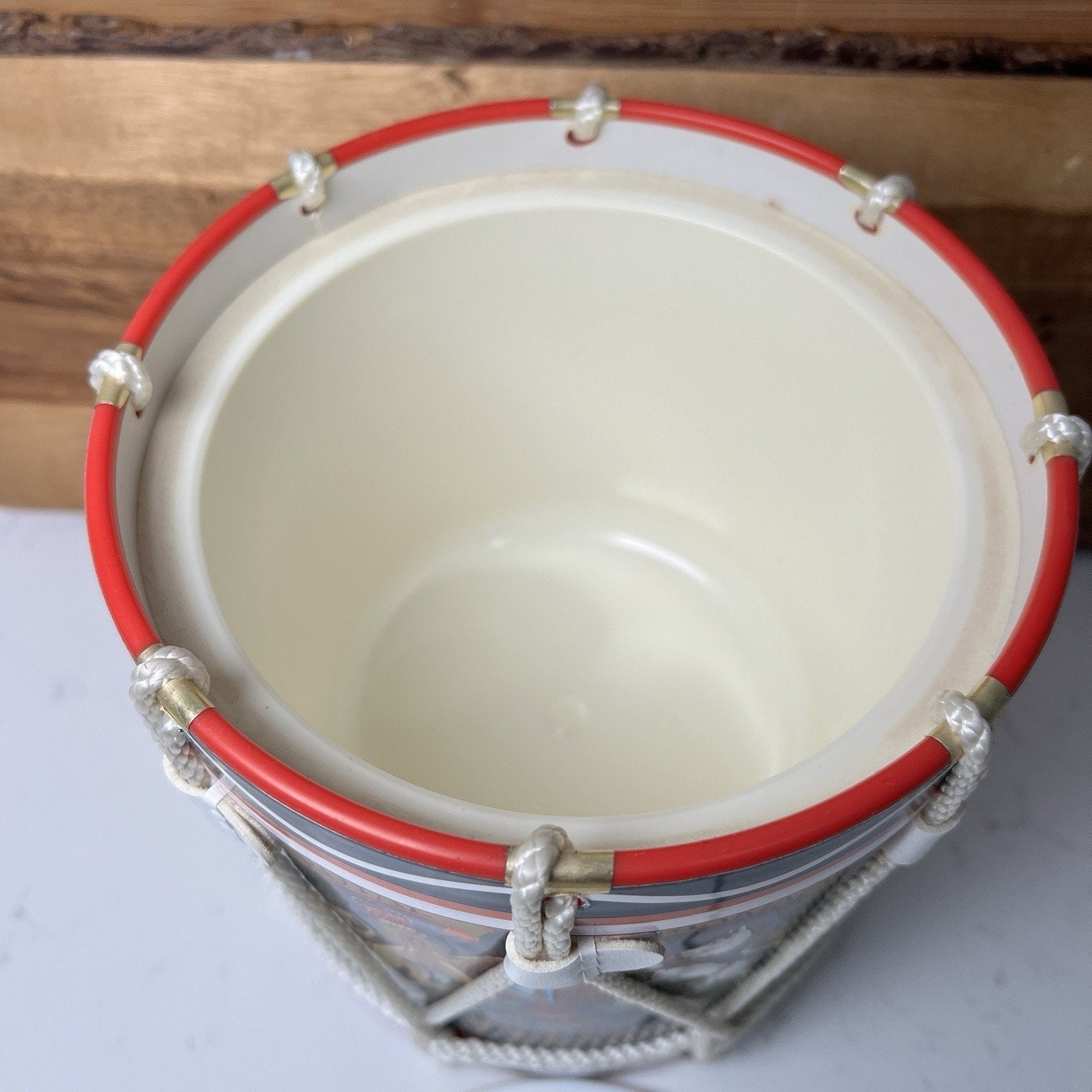 Small drum ice bucket with red rim and silver accents on a wooden surface