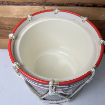 Small drum ice bucket with red rim and silver accents on a wooden surface