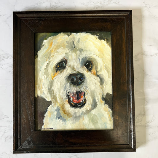 A framed custom pet portrait painting of a white fluffy dog, housed in a dark brown wooden frame, displayed on a light gray marble surface.
