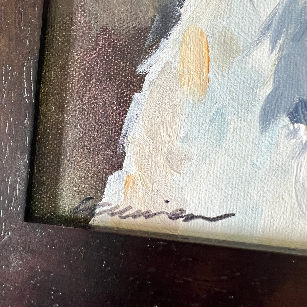 Close-up detail of a framed painting showing textured impasto brushstrokes in off-white, pale blue-gray, and warm beige, with a dark brown frame edge and a small dark signature near the bottom.