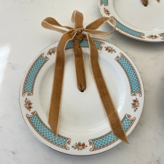White plate ornament with turquoise patterned border, small floral bouquets and a golden brown velvet bow