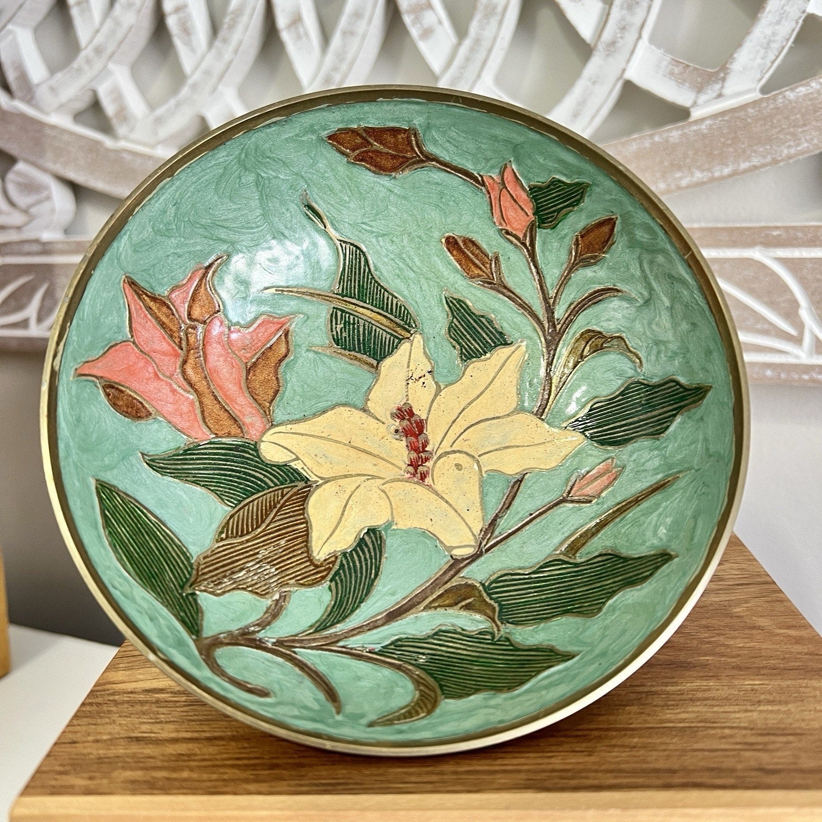Decorative brass bowl with floral design on a wooden stand
