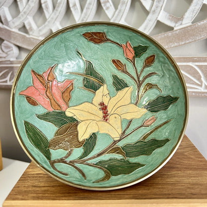 Decorative brass bowl with floral design on a wooden stand